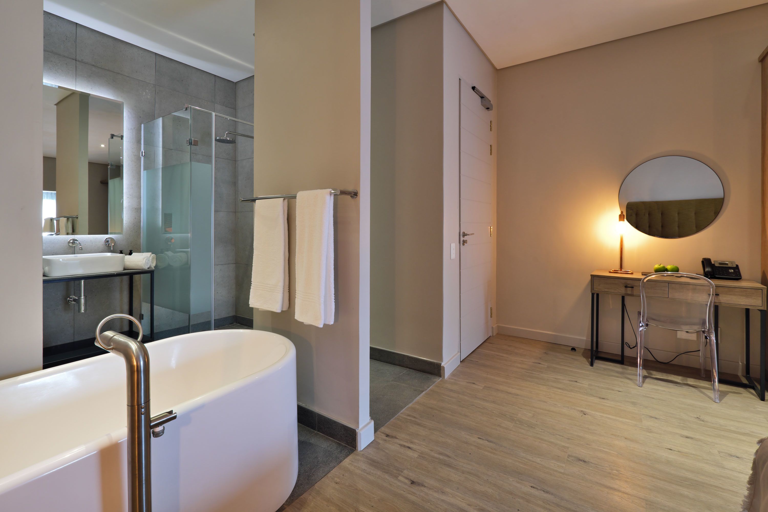 Un baño moderno con una bañera independiente, una ducha con cerramiento de vidrio, un tocador con espejo y un espejo redondo en la pared.