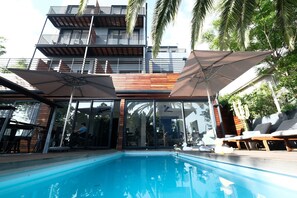 A modern building with a pool area, including lounge chairs and umbrellas. - The Tree House Boutique Hotel (Cape Town)