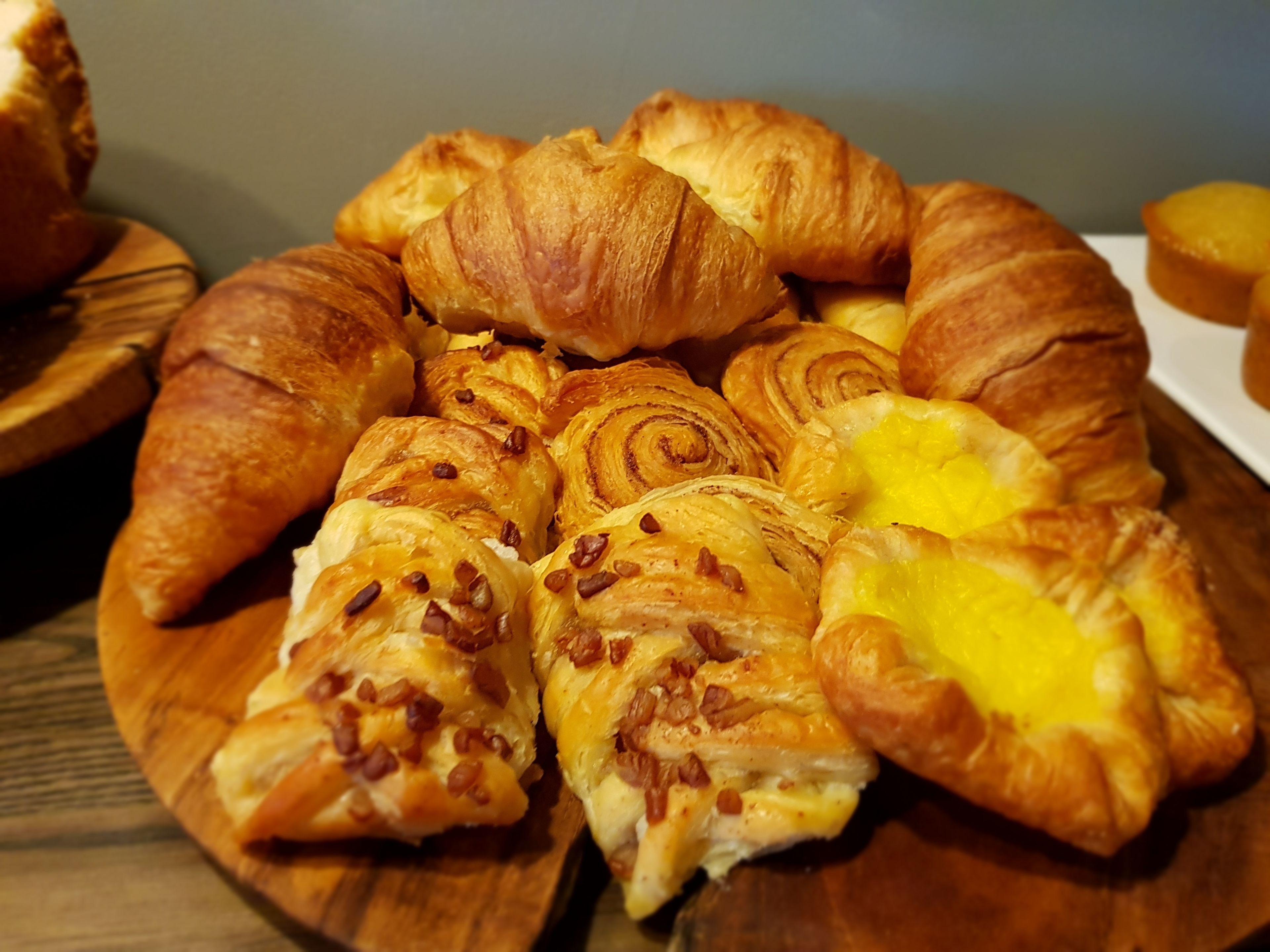 A wooden board with various pastries, including croissants and a pastry with a yellow filling.