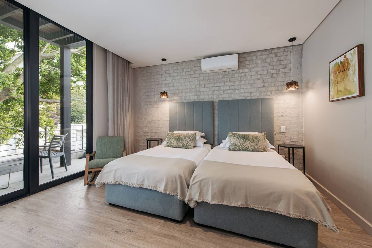 Een moderne slaapkamer met twee bedden, een groot raam en uitzicht op groen.