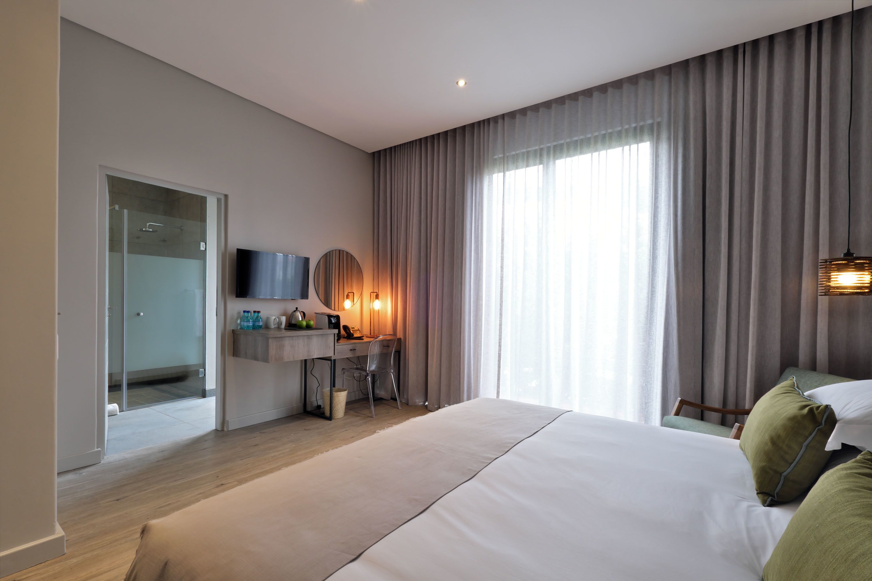A modern hotel room with a large bed, a desk with a chair, a television, and a shower area.