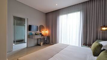 A modern hotel room with a large bed, a desk with a chair, a television, and a shower area.
