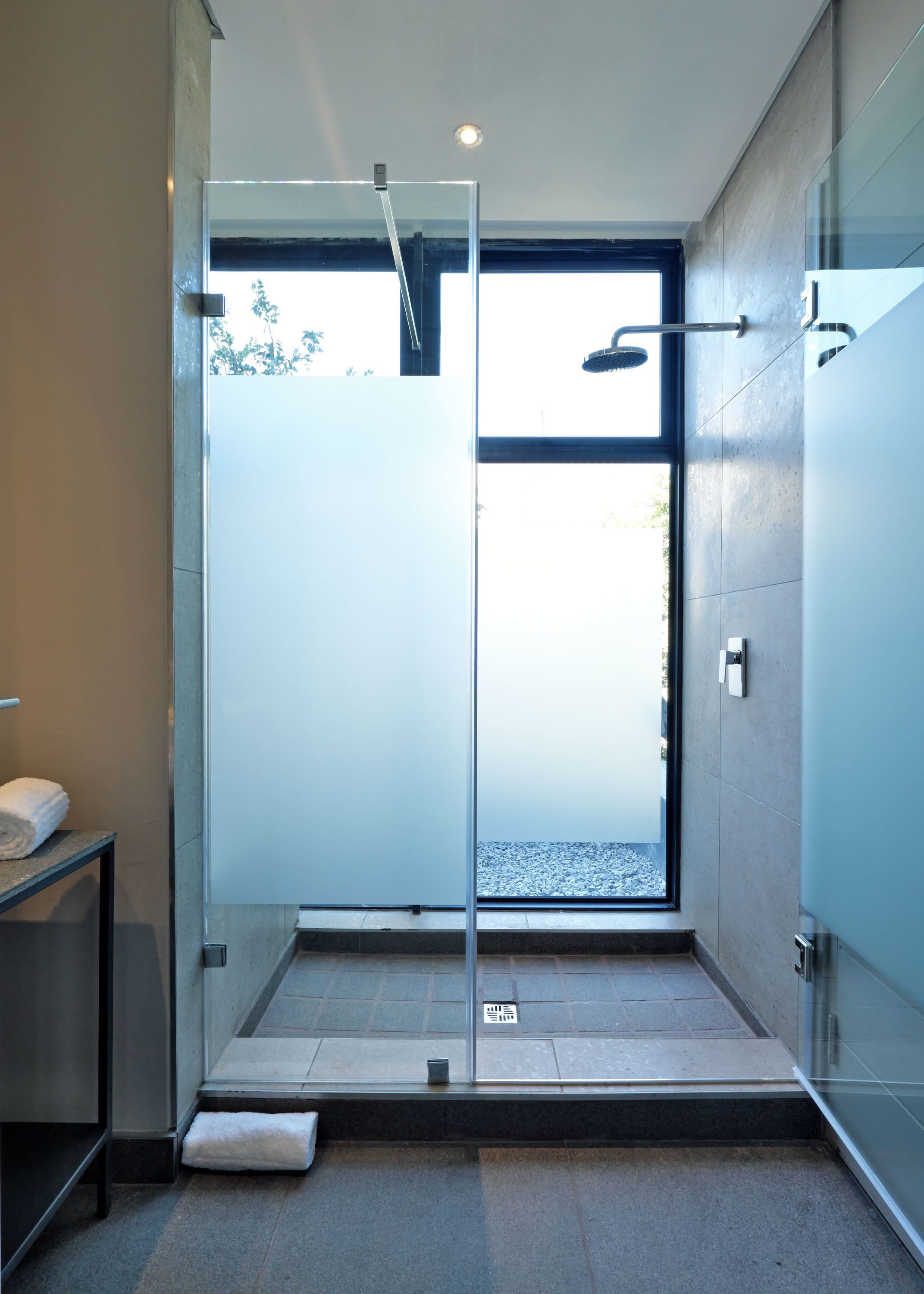 A modern shower area with a glass door, a towel on a shelf, and a view of the outdoors.