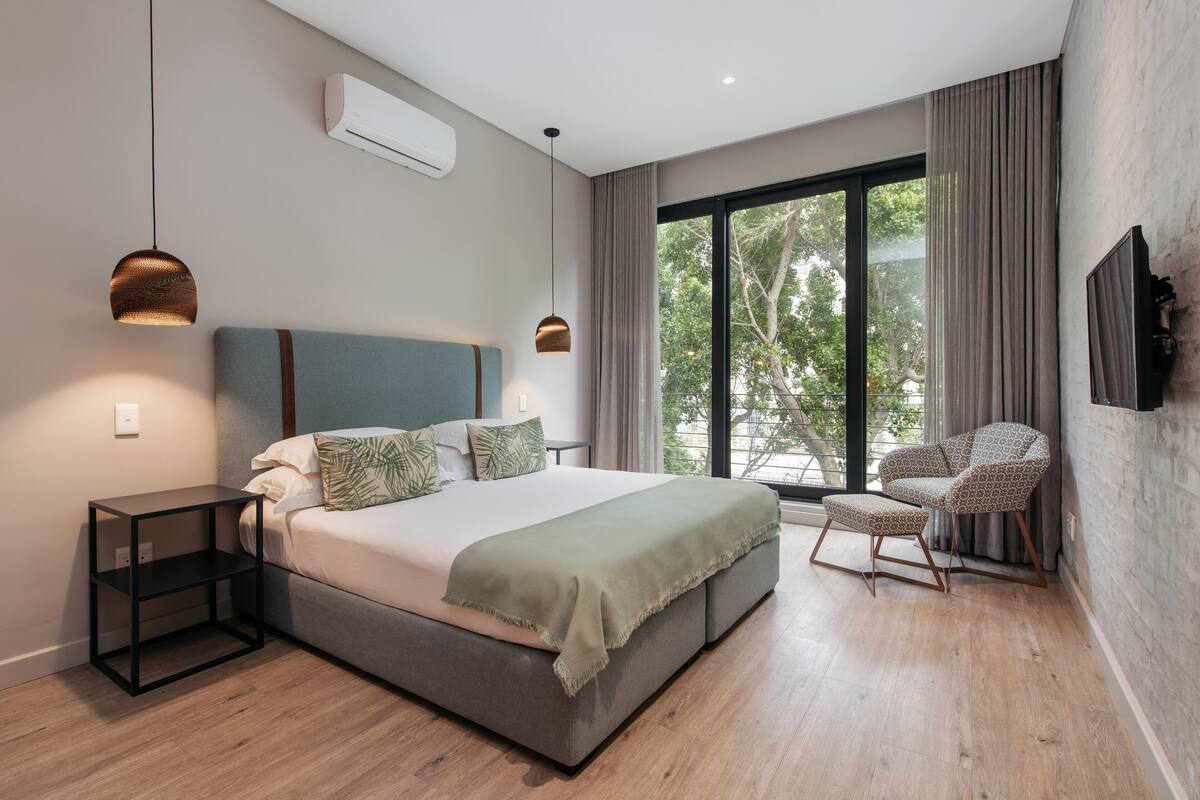 Een moderne slaapkamer met een groot bed, een nachtkastje, een stoel en een groot raam met gordijnen.