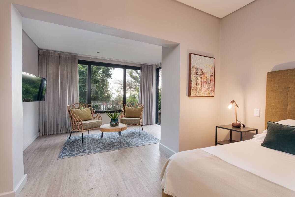 Een moderne hotelkamer met een groot bed, een zithoek met een tafel en stoelen, een flatscreen televisie en een groot raam met gordijnen.