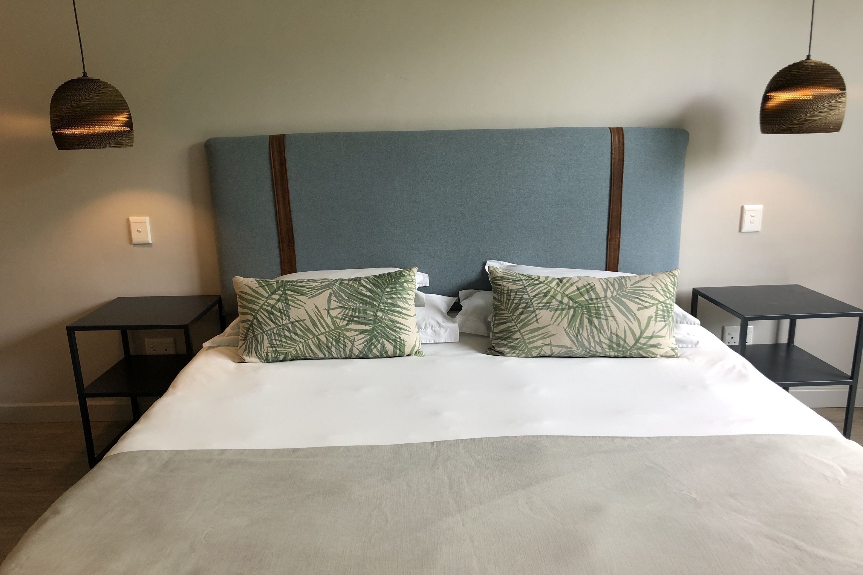 A neatly made bed with a blue headboard, two matching pillows, and two black nightstands.