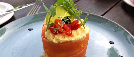 Une assiette avec une entrée de tartare de saumon, une tasse de café et un menu sur une table à l’extérieur.