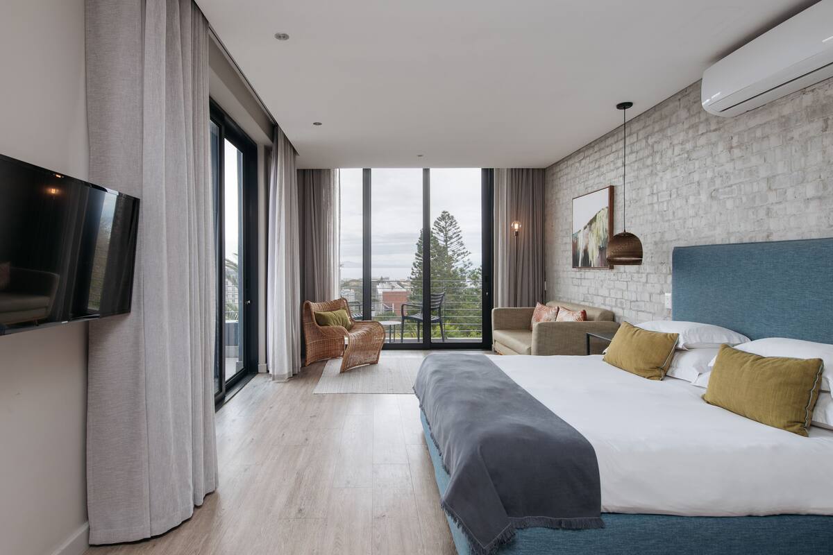 Een moderne hotelkamer met een groot bed, een flatscreen televisie, een bank en uitzicht op de stad door grote ramen.