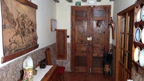 A rustic interior with a wooden door marked "SALIDA EXIT," a dining area with a table and chairs, and a shelf with plates. - Casa Rural el Rincon del Infante (Villa de Don Fadrique)