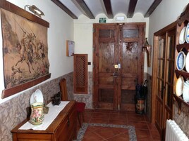 Un interior rústico con una puerta de madera que indica “SALIDA EXIT”, un comedor con una mesa y sillas, y una estantería con platos.
