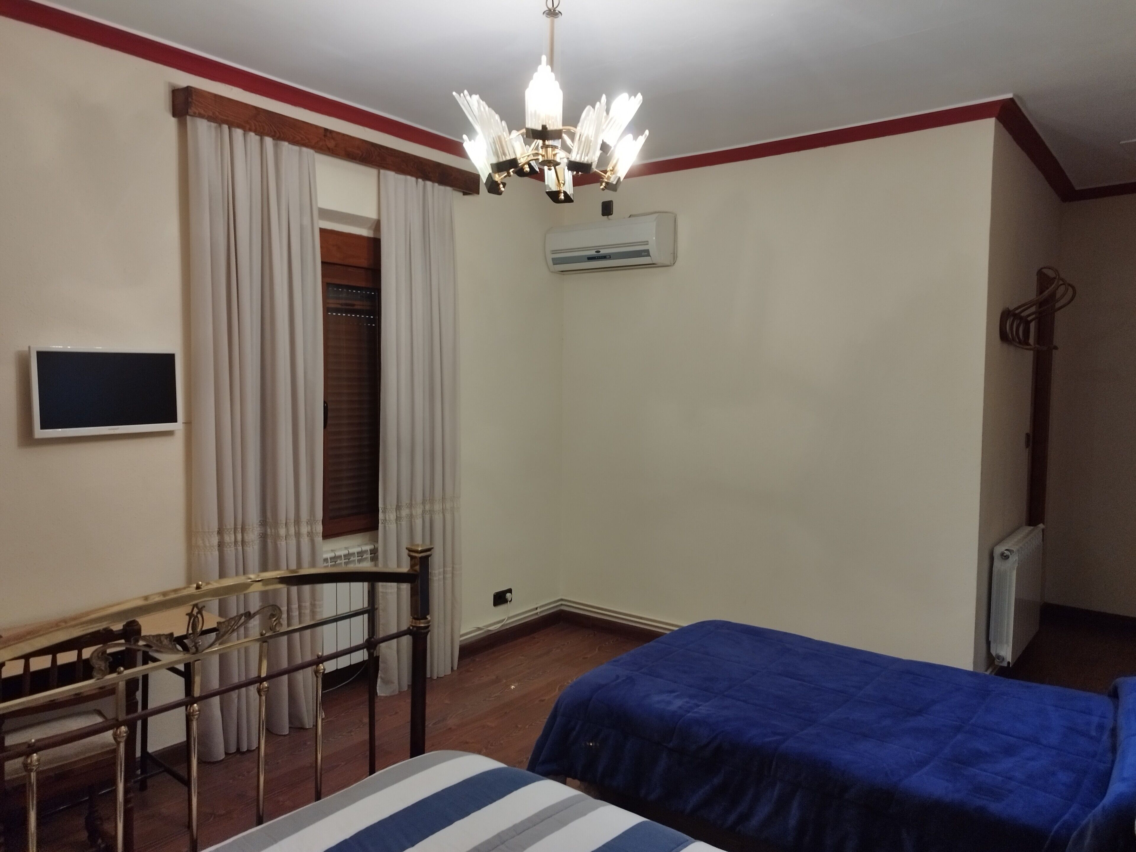 Una camera d'albergo con un letto, una scrivania con sedia, una televisione, un lampadario e un condizionatore d'aria.