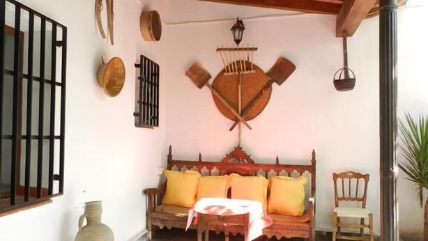 A cozy patio with a wooden bench, a table, and a decorative wall hanging. - Casa Rural el Rincon del Infante (Villa de Don Fadrique)