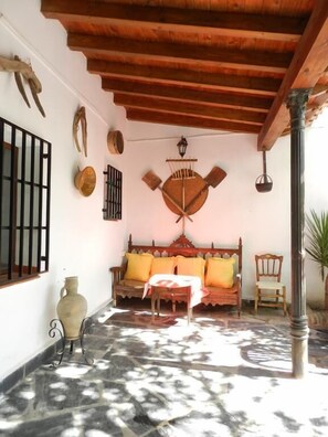 A cozy patio with a wooden bench, a table, and a decorative wall hanging. - Casa Rural el Rincon del Infante (Villa de Don Fadrique)