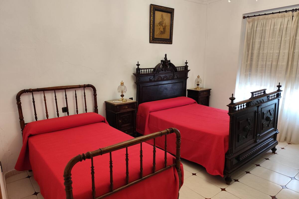 Une chambre à coucher avec deux lits en bois, une commode en bois foncé, une petite table de chevet avec une lampe et un tableau encadré accroché au mur.