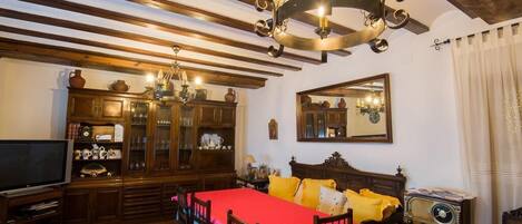 A traditional room with a wooden ceiling, a bed with yellow bedding, a wooden cabinet with glass doors, a television, and a vintage radio.