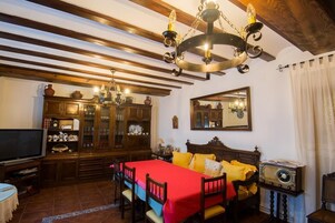 Una habitación tradicional con techo de madera, una cama con ropa de cama amarilla, un mueble de madera con puertas de cristal, un televisor y una radio antigua.