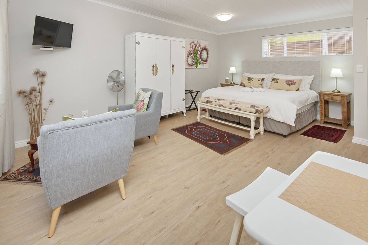 A bedroom with a bed, a chair, a wardrobe, a TV, and a window with blinds.