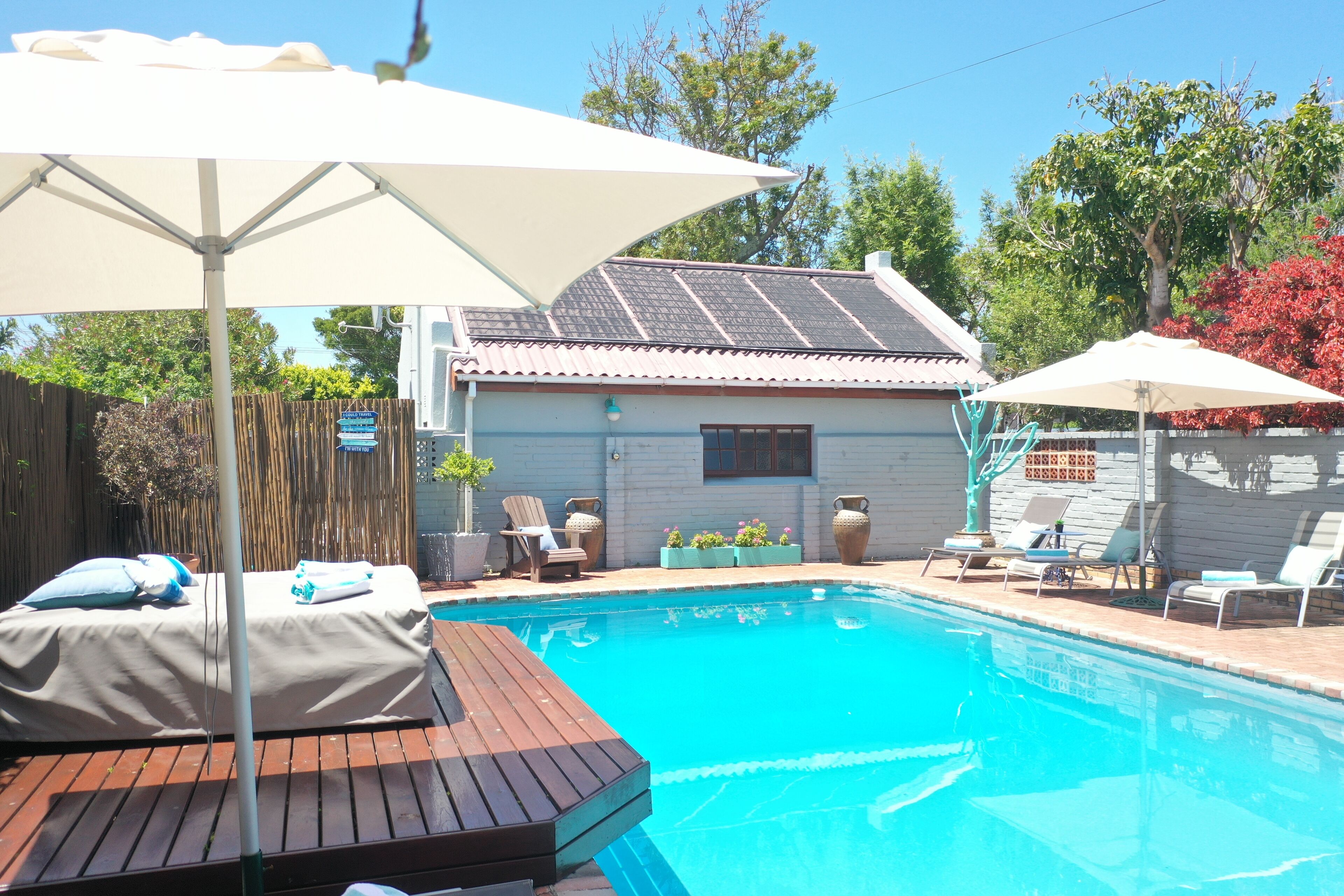 A swimming pool with a wooden deck, lounge chairs, and umbrellas.