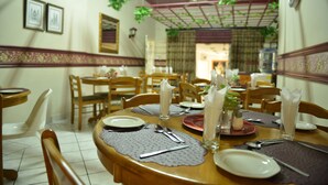 A dining area with wooden tables and chairs, neatly set with plates, cutlery, and glasses. - Rita Guest House (Abaqulusi)