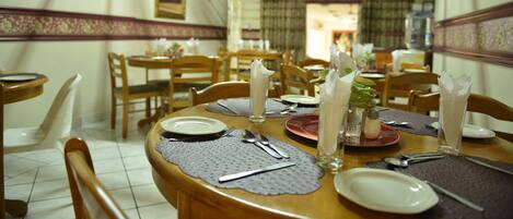 A dining area with wooden tables and chairs, neatly set with plates, cutlery, and glasses.
