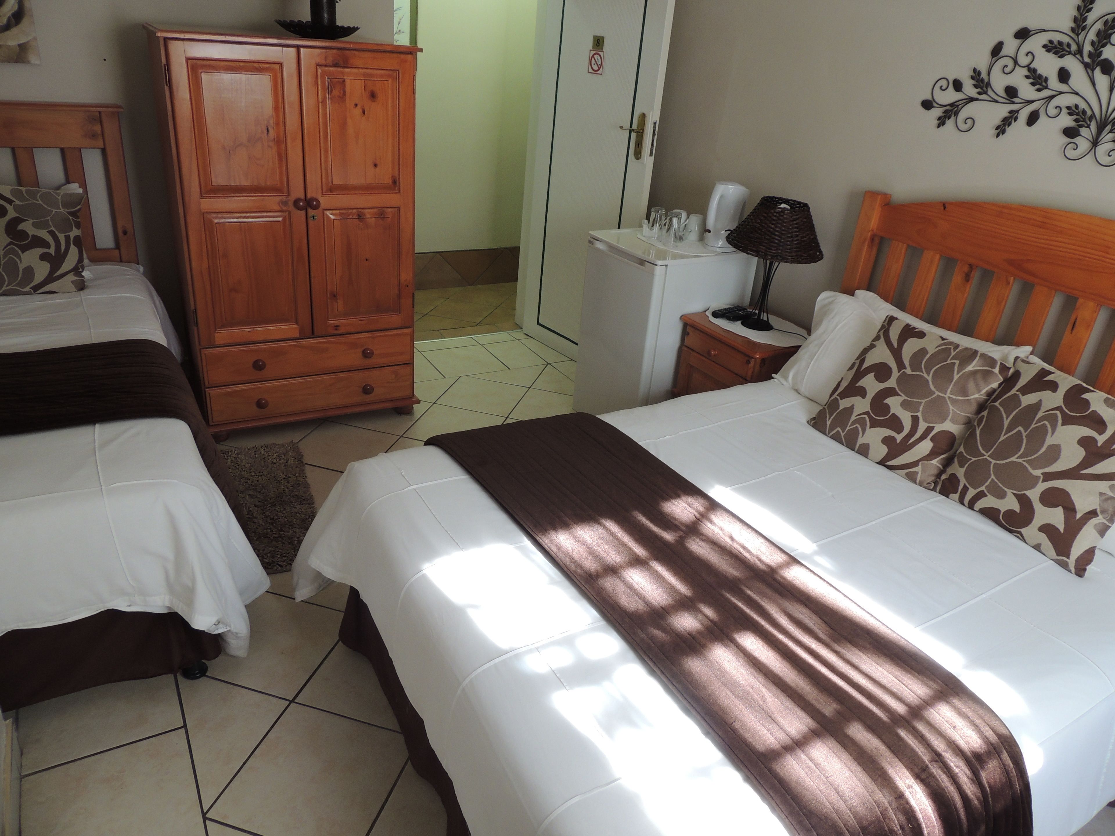Una habitación de hotel con dos camas, un armario de madera, una mesita de noche con lámpara y un adorno en la pared.
