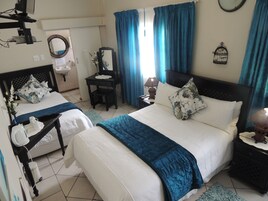 Quarto de hotel com duas camas, uma escrivaninha, uma cadeira, um abajur e uma janela com cortinas.