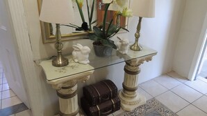 A glass-top console table with two lamps, a potted plant, a white rabbit figurine, and a vintage suitcase. - Rita Guest House (Abaqulusi)