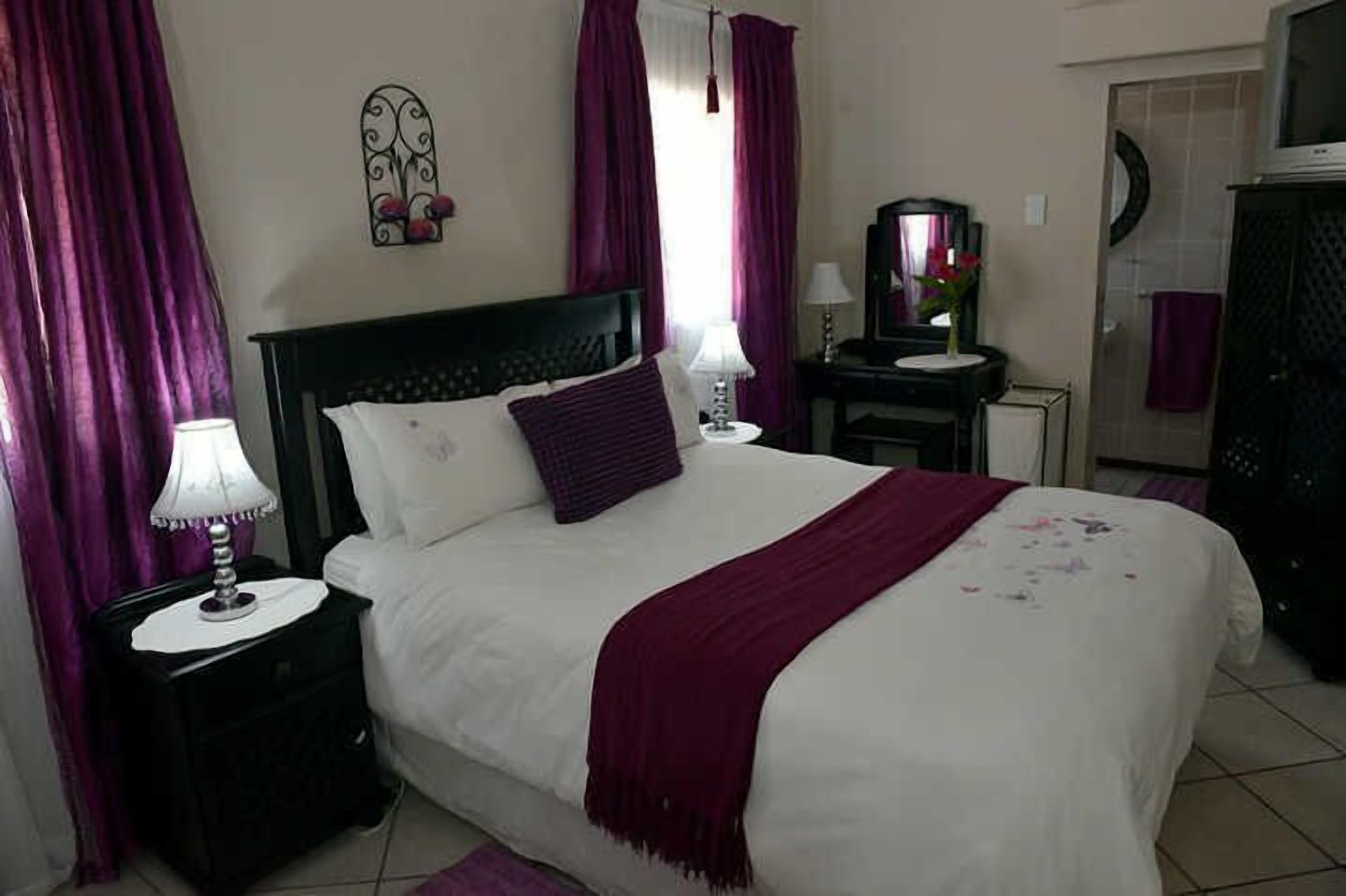 Un dormitorio con cama, mesitas de noche, un espejo y una ventana con cortinas.