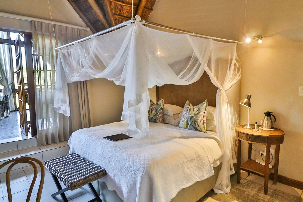 Quarto com cama de dossel, mesa de cabeceira com abajur e uma cadeira.