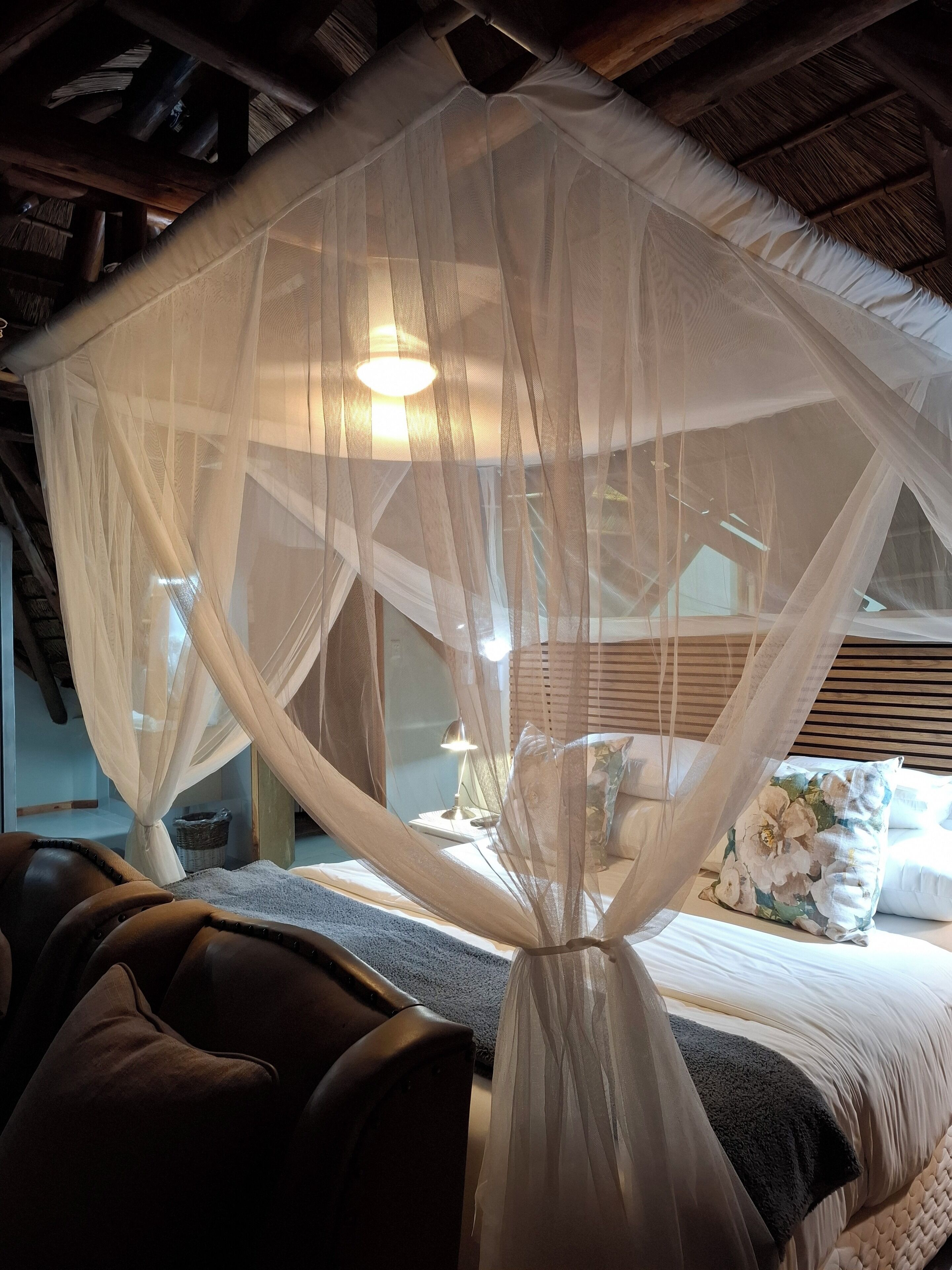 A bedroom with a canopy bed, wooden headboard, and a nightstand with a lamp.