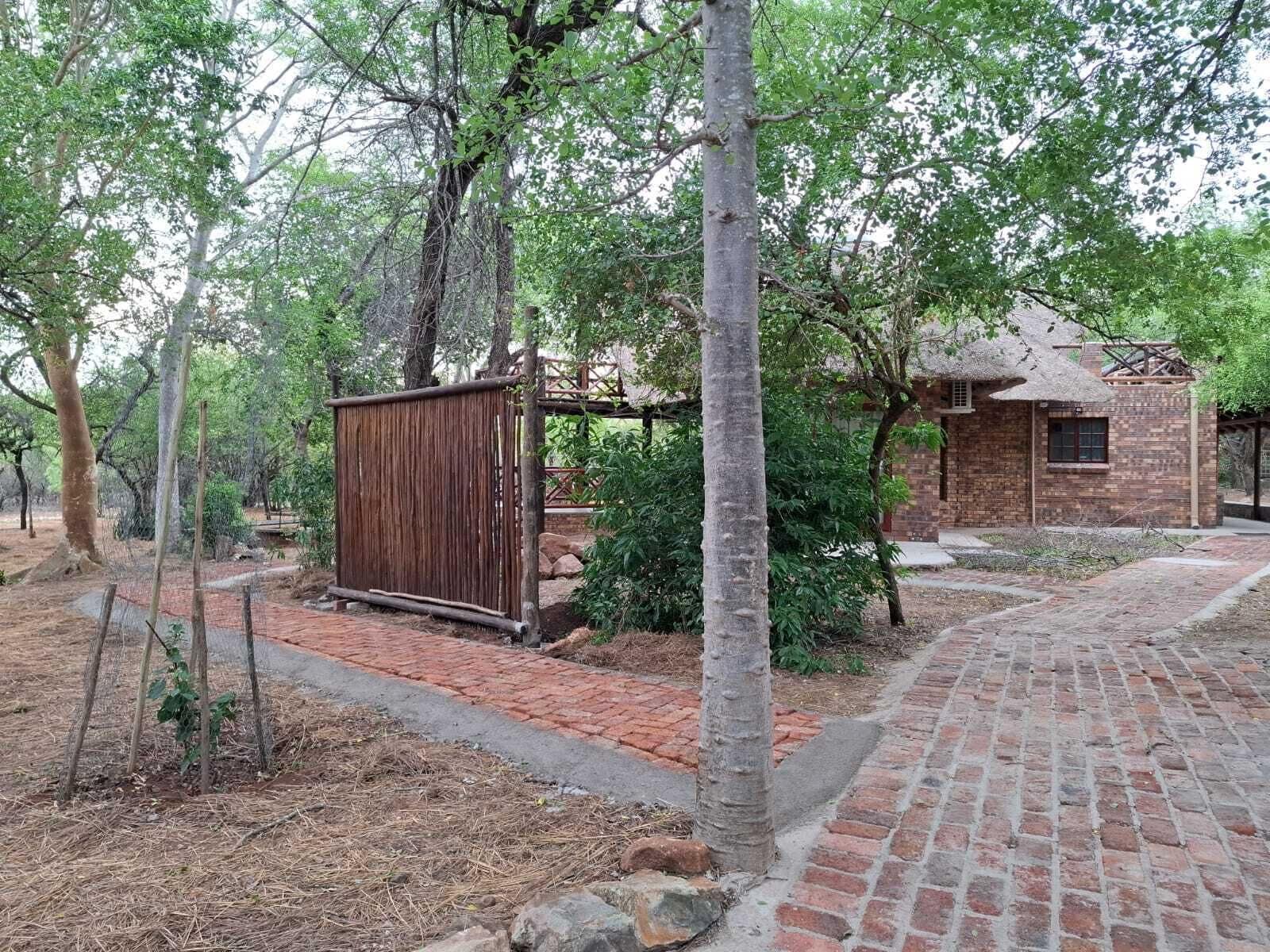 A rustic building with a thatched roof, surrounded by trees and a brick pathway.
