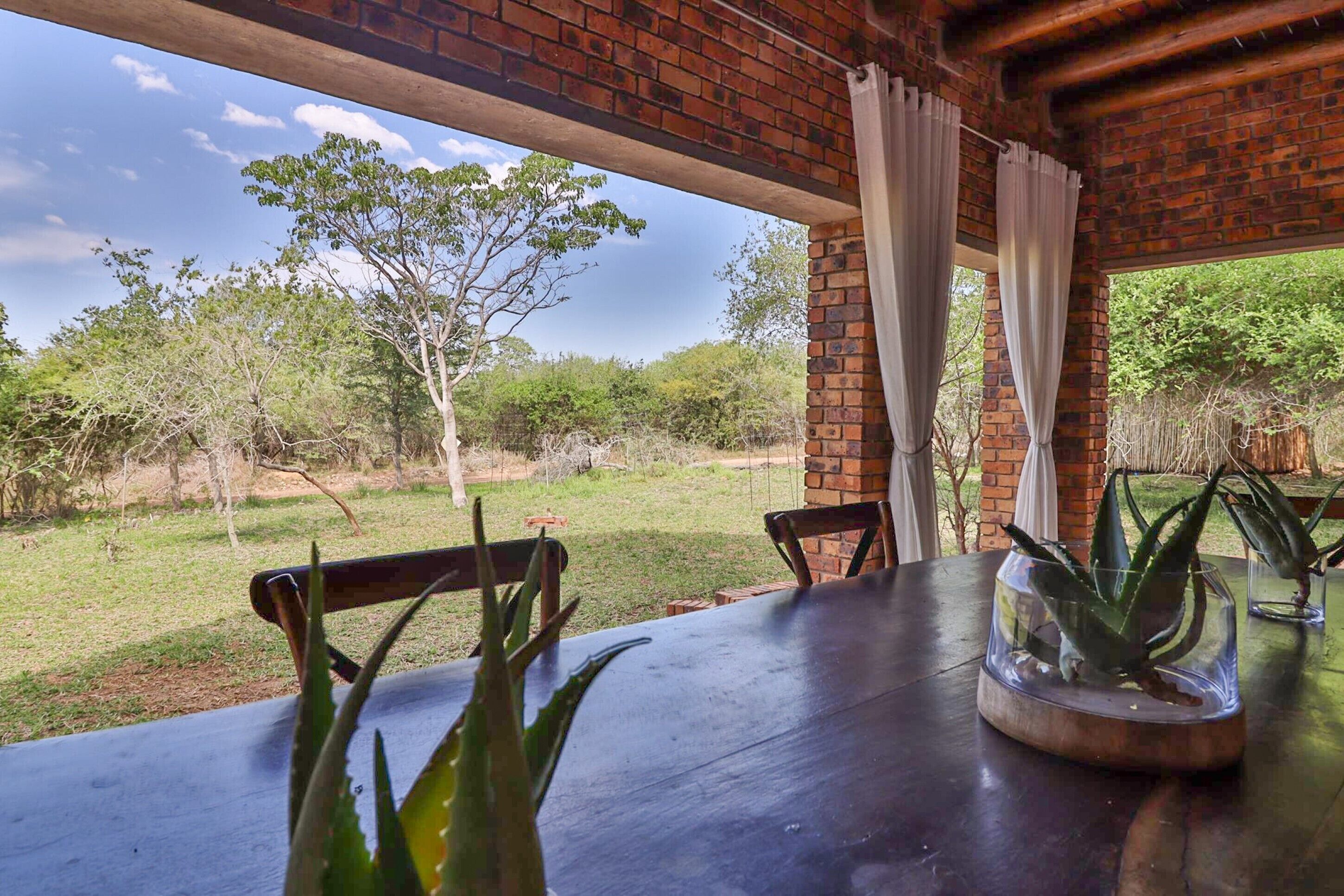 A dining area with a brick ceiling, a table with chairs, and a view of a grassy landscape with trees.