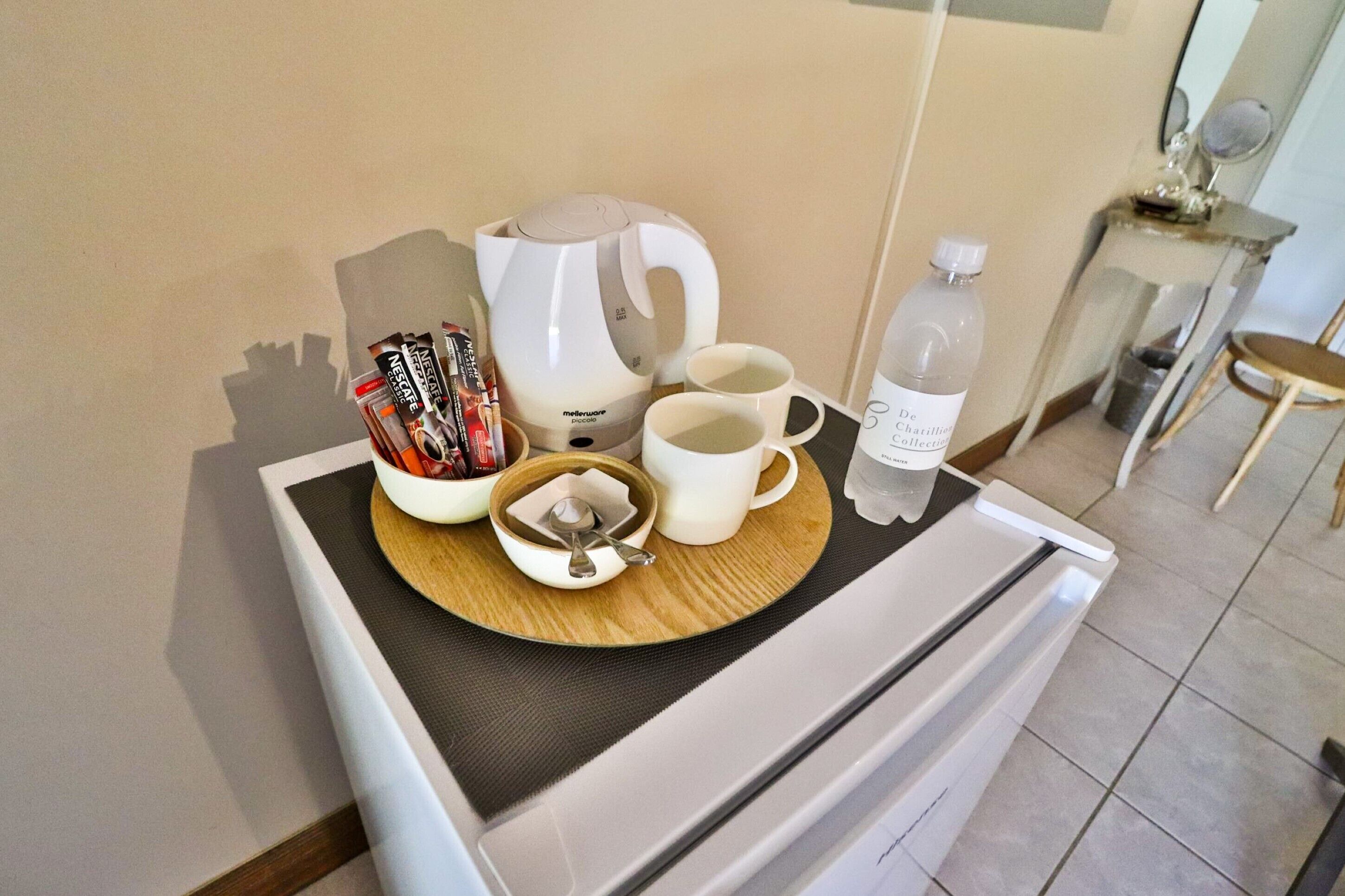 Un plateau préparé pour le petit-déjeuner, avec une machine à café, deux tasses, une bouteille d’eau et un récipient contenant des capsules Nespresso.