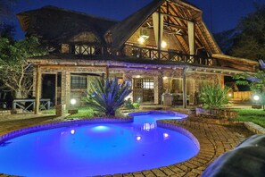 A large, rustic building with a thatched roof and a swimming pool area.