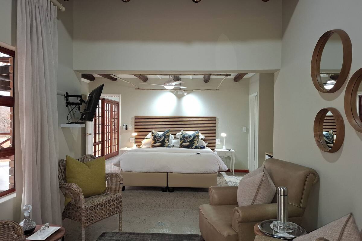 Um quarto com uma cama, duas cadeiras, uma mesa de cabeceira, um espelho e um ventilador de teto.