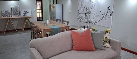 Una sala de estar con sofá, mesa de comedor y una gran obra de arte en la pared.