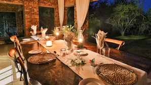A dining table set for a meal with candles, vases with flowers, and a view of trees outside. - Kruger Riverside Lodge (Nkomazi)