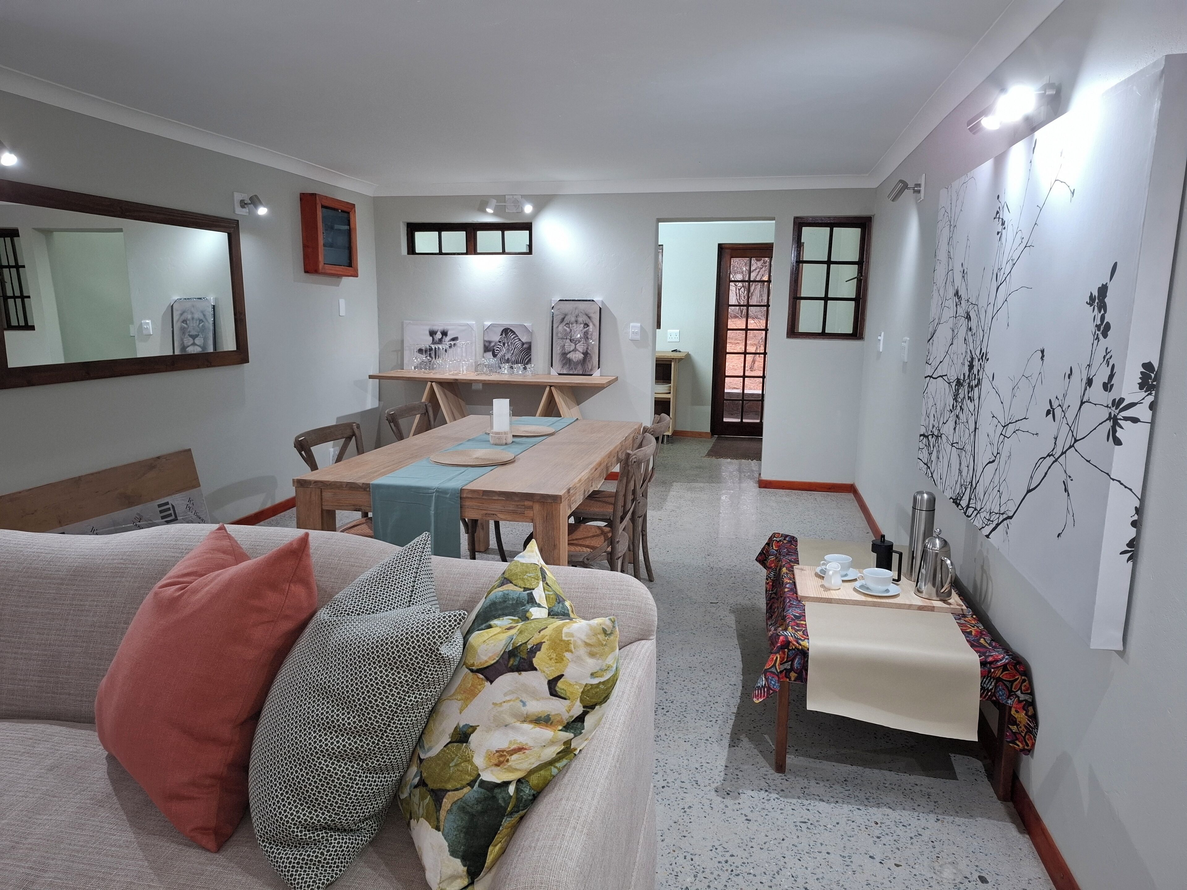 Un salon comprenant un canapé, une table à manger et une petite table sur laquelle se trouvent des tasses et un thermos. Une porte donne accès à une autre pièce.
