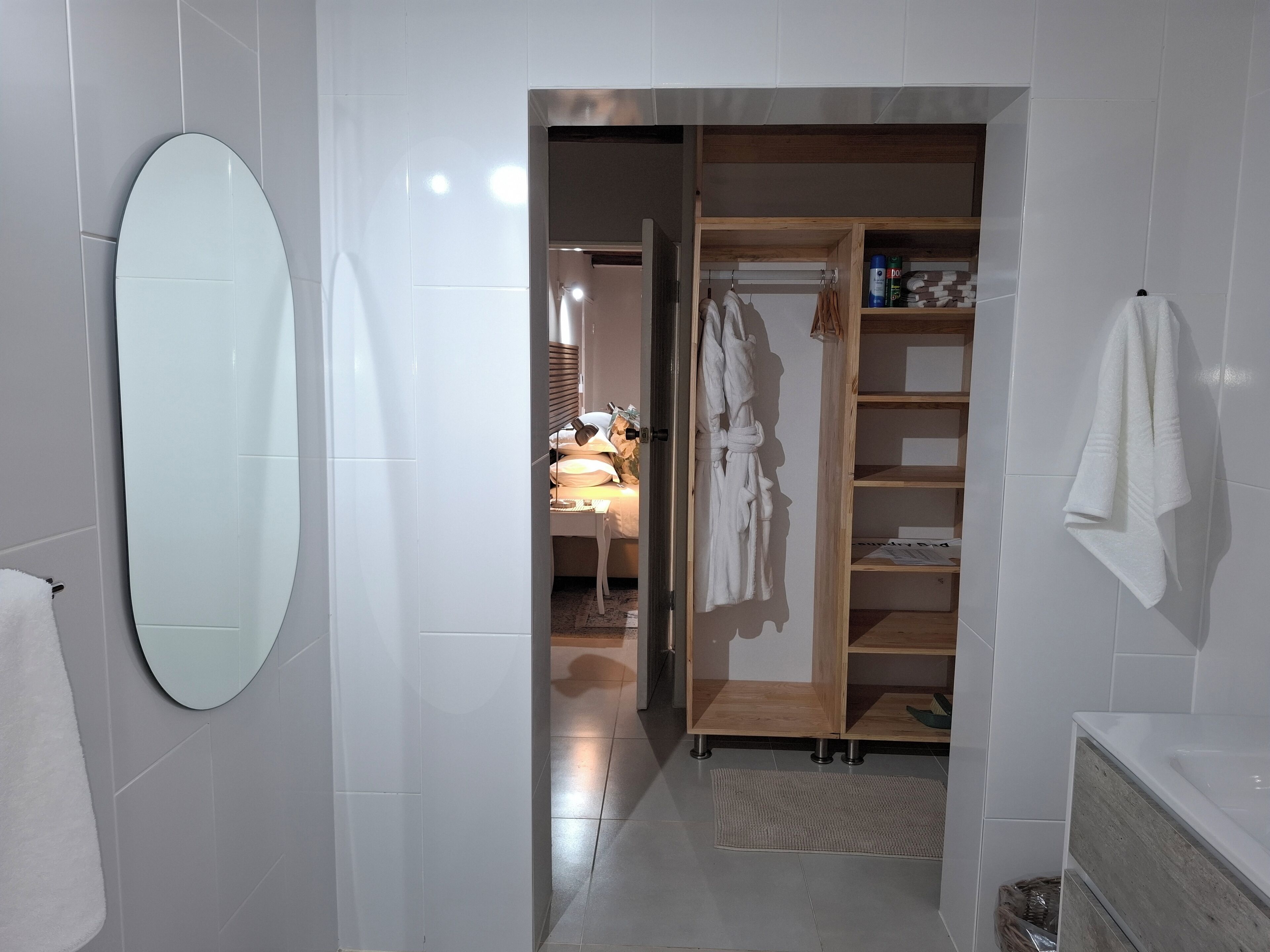 Een moderne badkamer met een grote, ovale spiegel, een houten garderobe en een witte handdoek aan de muur.