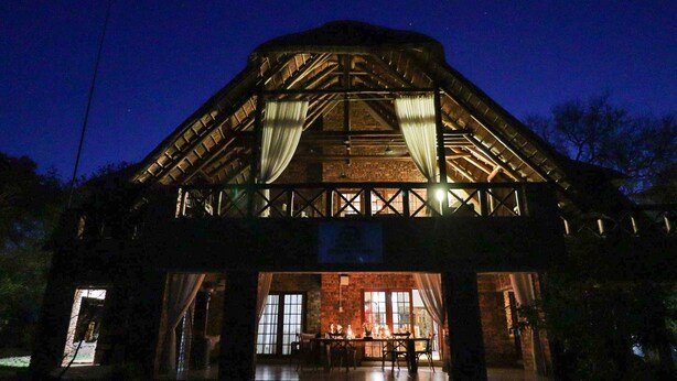 A rustic building with a brick facade and large windows, featuring a dining area with tables and chairs. - Kruger Riverside Lodge (Nkomazi)