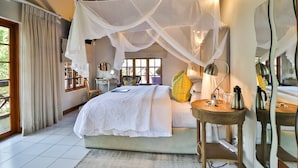 A bedroom with a canopy bed, bedside table, lamp, and a view of the outdoors. - Kruger Riverside Lodge (Nkomazi)
