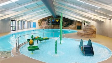 An indoor swimming pool with slides and a rock formation backdrop.