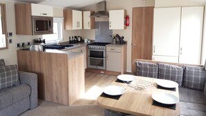 A compact kitchen with a central island, built-in microwave, stove, oven, and a small dining area with a table and chairs. - St Ives Holiday Village (St Ives)