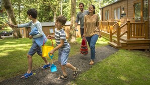A family walking towards a wooden cabin with a deck and a small porch. - St Ives Holiday Village (St Ives)