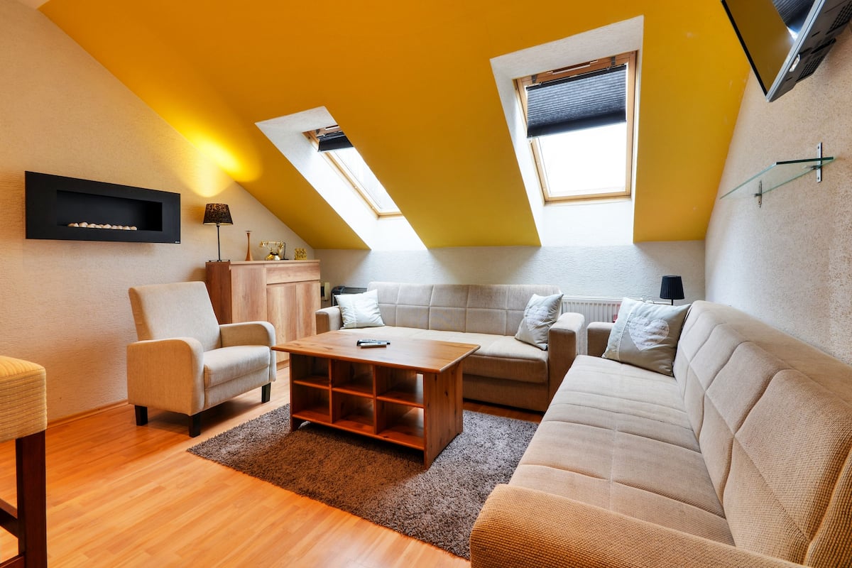 Een modern loft appartement met een schuine plafond, ingebouwde planken, een bank, een salontafel en een aan de muur bevestigde televisie.