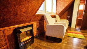 A cozy attic room with a fireplace, wooden walls, and a seating area with chairs. - Apart & Wellness Hotel VILLA IVICA  (Marianka)