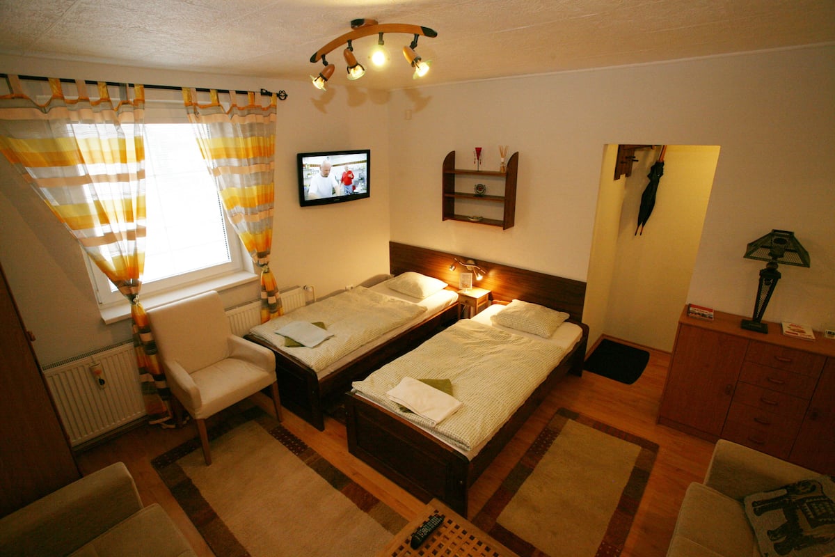 Een kamer met twee bedden, een stoel, een televisie, een plank met spullen en een lamp.