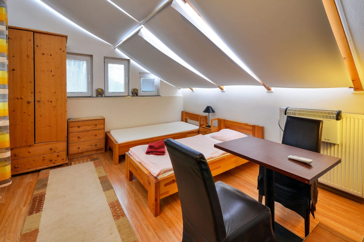 Een ruime, goed verlichte kamer met een bed, bureau, stoel, kledingkast en radiator.
