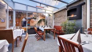 An outdoor patio with tables and chairs, a glass enclosure, and a stone wall with a fireplace. - Apart & Wellness Hotel VILLA IVICA  (Marianka)