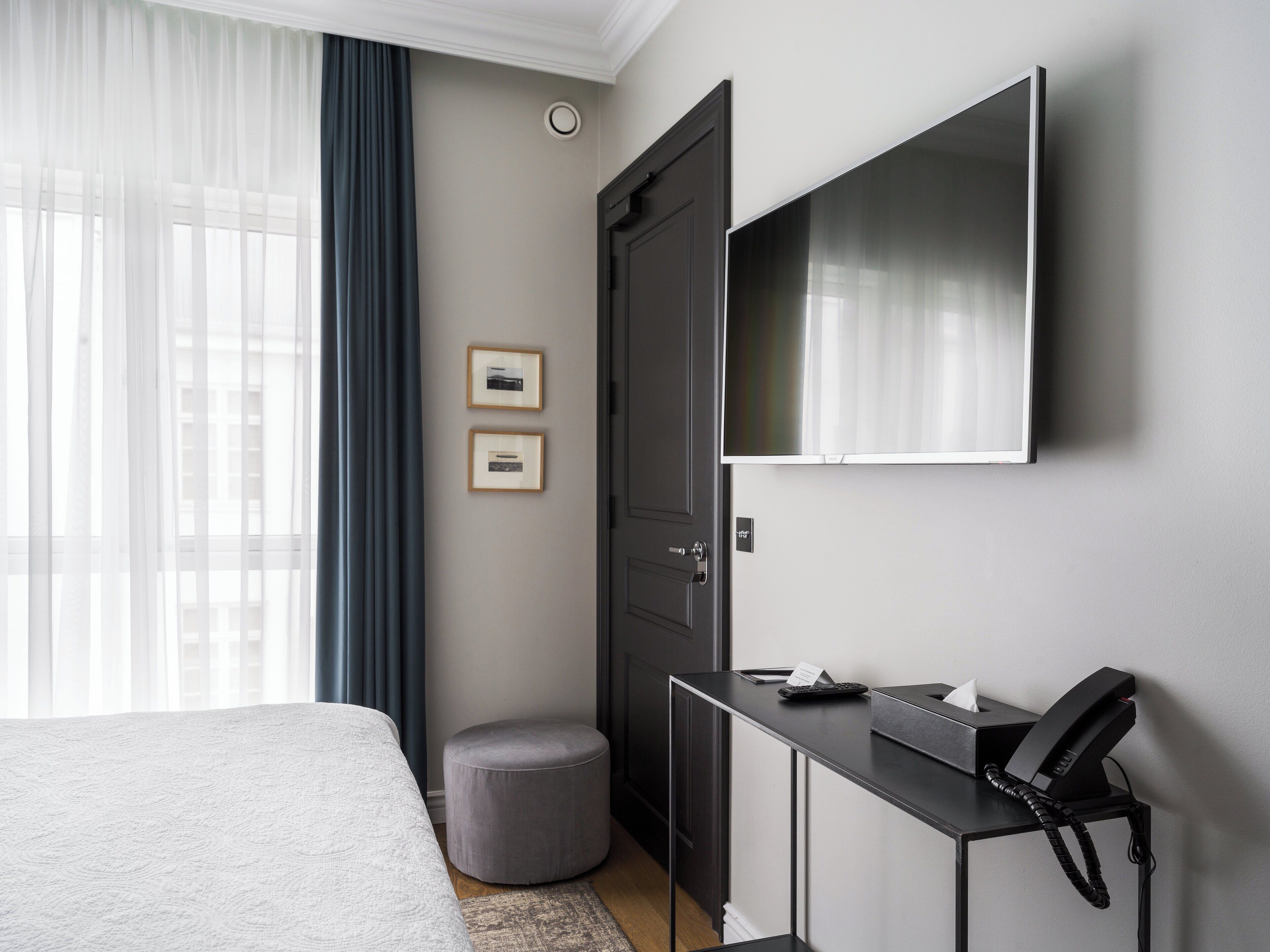 A hotel room with a bed, a desk with a telephone, a television, and a small ottoman.